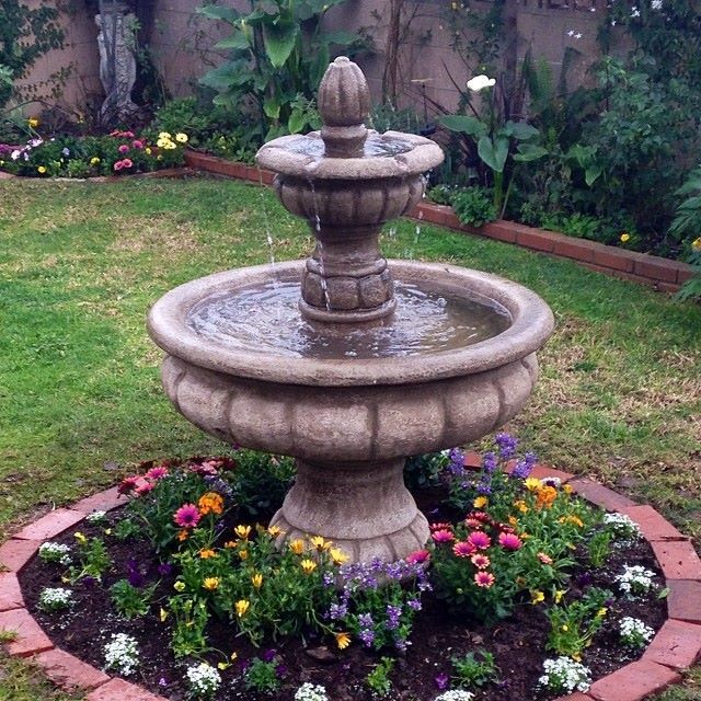 Two-tier stone garden fountain surrounded by flowers